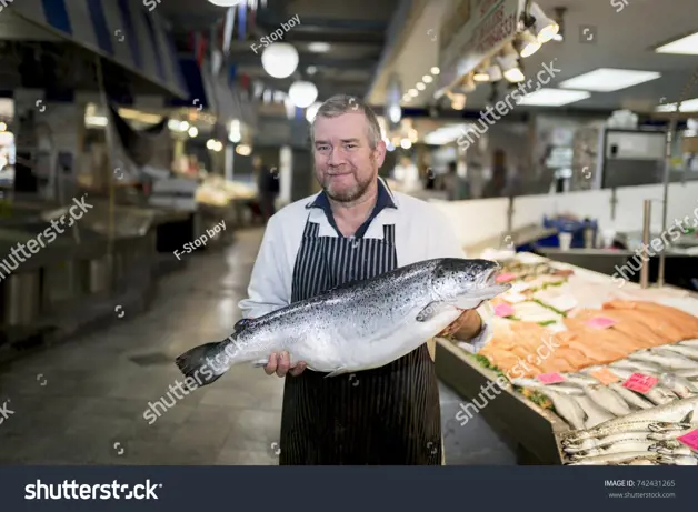 Stock Photo Male Fishmonger Wearing An Apron Holding Large And Whole Salmon Fish In Front Of Display Counter 742431265